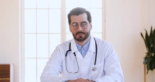 Professional male doctor physician in white medical uniform speaking looking at camera make video chat conference call or recording healthcare webinar training talk to distant patient, webcam view
