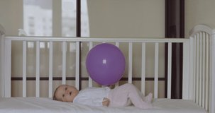 Caucasian baby laying on bed and playing with balloon in her hand. RAW Graded footage 4K slow motion 50fps