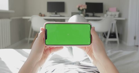New York, USA - February 18, 2020: Woman use of smartphone with green screen, chroma key. iPhone X or XS Max, 11 Pro Max horizontal orientation, modern apartment interior background. POV. 