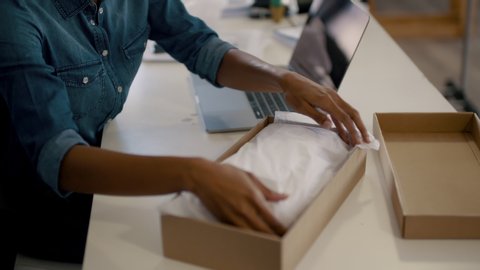 Online store owner working at her desk folding a document placing it in the box and packing the order for shipping to customer. ecommerce business entrepreneur preparing a package for delivery.
