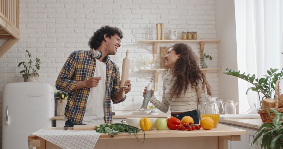 Fun young couple with curly hair dancing and singing while cooking in the kitchen, spending time together - recreational pursuit slow motion  Royalty-Free Stock Footage #1047026584
