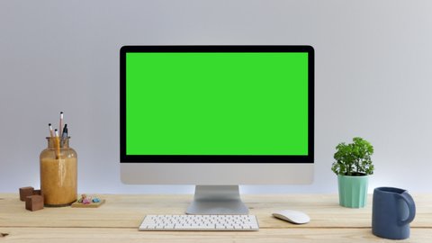 Computer desktop with mock-up green screen on wood table with grey background in office, Zoom shoulder view.