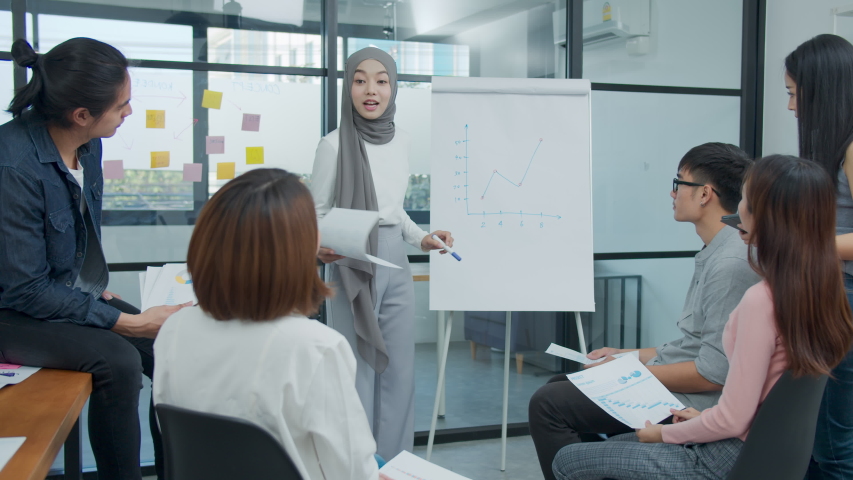 Young asian muslim presenting data results sale marketing on board in office. Asia woman show forcast plan and ideas to business partner or colleagues group enjoy teamwork in small office Royalty-Free Stock Footage #1047029473