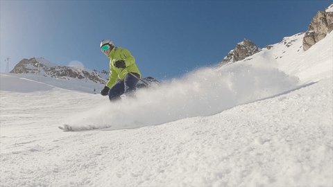Super slow motion shot of a young man skiing in the Swiss alps. Skier carving and spraying snow at camera