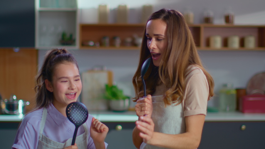 Smiling mother and daughter singing in spoons on modern kitchen in slow motion. Joyful woman and girl cooking on kitchen. Happy family having fun together at home Royalty-Free Stock Footage #1047031669