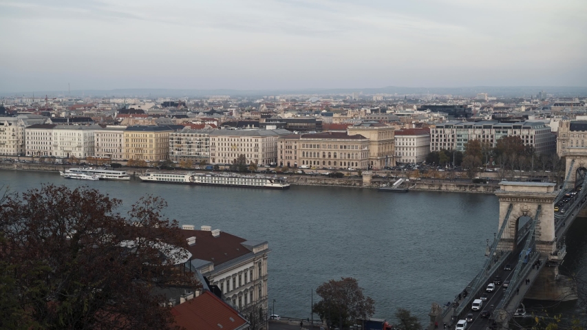Gimbal pan shot from left to right of Chain Bridge and river Danube shot from above, Gresham Palace in Budapest in winter time. Pest cityscape shot from Buda