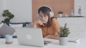 Attractive Young Asian Student looking at laptop screen wear headphones learning online on internet, listening online teacher, watching video tutorial and researching. Education and E-Learning Concept