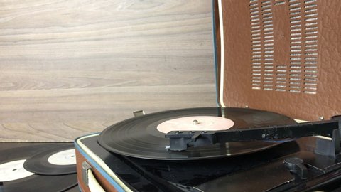 Old turntable with a phonograph record. Playback in progress. The pickup with the needle rises after playback ends. The man puts him on the stand and turns off the playback. The rotation stops