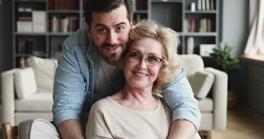 Smiling 30s young adult man grown handsome son looking at camera hugging old mature 60s mom expressing love and care embracing cuddling on mothers day concept. 2 generations family closeup portrait Royalty-Free Stock Footage #1047036838