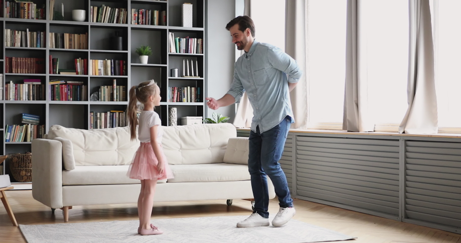 Affectionate loving young dad teaching dancing with cute small child. Daughter princess wear crown skirt having fun in modern living room playing ball together enjoy sweet funny activity at home. Royalty-Free Stock Footage #1047036856