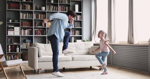 Active cheerful young adult dad dancing having fun with small kid daughter imitate father moves at home, happy parent daddy and cute little girl play together indoors