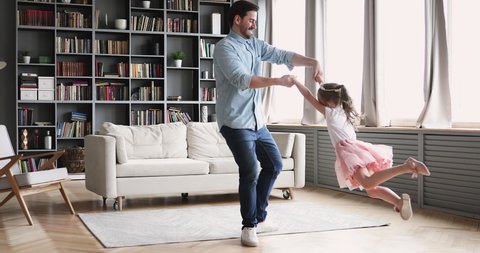 Loving father having fun spinning dancing with cute little child daughter princess wear crown in modern living room. Happy dad and small kid girl playing enjoying funny active dance together at home