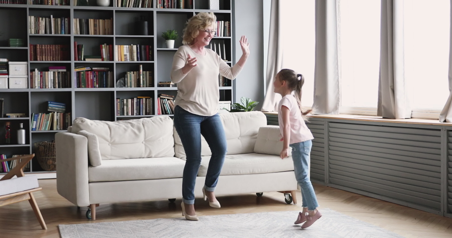 Funny small girl granddaughter dance with old grandma babysitter in living room. Happy two 2 generations active family senior nanny and cute energetic grandkid  enjoy time together at home Royalty-Free Stock Footage #1047036880