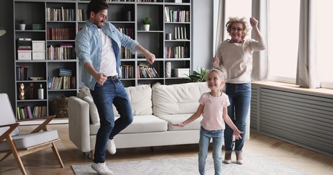 Happy funny multigenerational family 3 age generations having fun dance together in living room, cute girl daughter granddaughter. Old grandmother and young son father enjoy lifestyle activity at home
