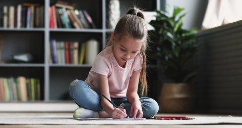 Cute concentrated little kid girl draw color pencil play alone on floor. Pretty preschool child coloring picture at home enjoy creative activity relax sit on carpet, children playtime education concep