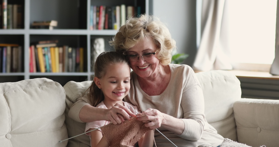 Happy senior old adult granny teaching small cute granddaughter learning knitting needles.Two generations family grandparent and little grandchild, having fun enjoying handcraft hobby concept at home Royalty-Free Stock Footage #1047036922