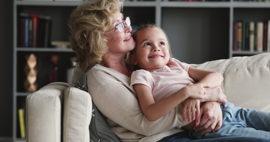Happy relaxed older adult granny embracing preschool child granddaughter cuddling bonding rest on couch at home. Affectionate 2 two age generations family grandparent and grandkid enjoy time together Royalty-Free Stock Footage #1047036928