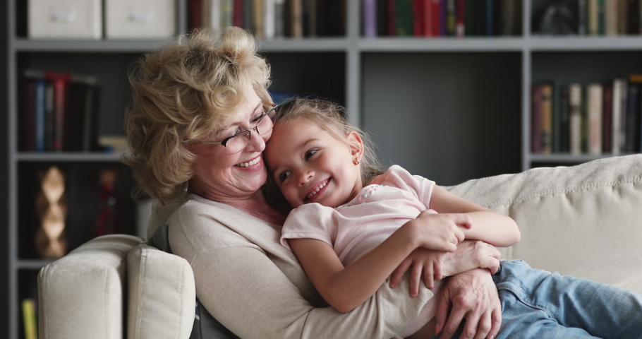 Happy relaxed older adult granny embracing preschool child granddaughter cuddling bonding rest on couch at home. Affectionate 2 two age generations family grandparent and grandkid enjoy time together | Shutterstock HD Video #1047036928