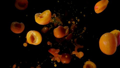 Delicious ripe apricot halves are flying up with a splashes of juice on a black background in slow motion