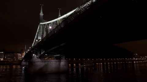 BUDAPEST, HUNGARY – DECEMBER 10, 2019: Pan shot left to right of Liberty bridge in Budapest at night time, under black dark sky in winter time. Dunab river and Budapest bridge in dark night