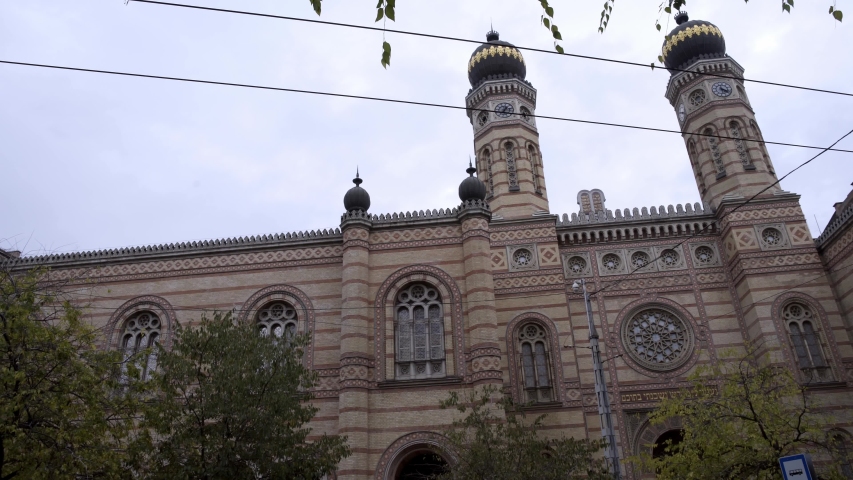 Gimbal pan shot left to right of the Dohany Street Synagogue in Budapest under cloudy sky with wires above. December daylight, view of Synagogue in Hungary