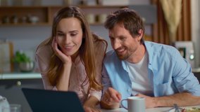 Portrait of businesswoman and businessman using laptop on domestic kitchen together. Happy man having breakfast before work at home. Cheerful wife bringing husband tea on kitchen in slow motion - Powered by Shutterstock - Get 15% off with code: PIKWIZARD15
