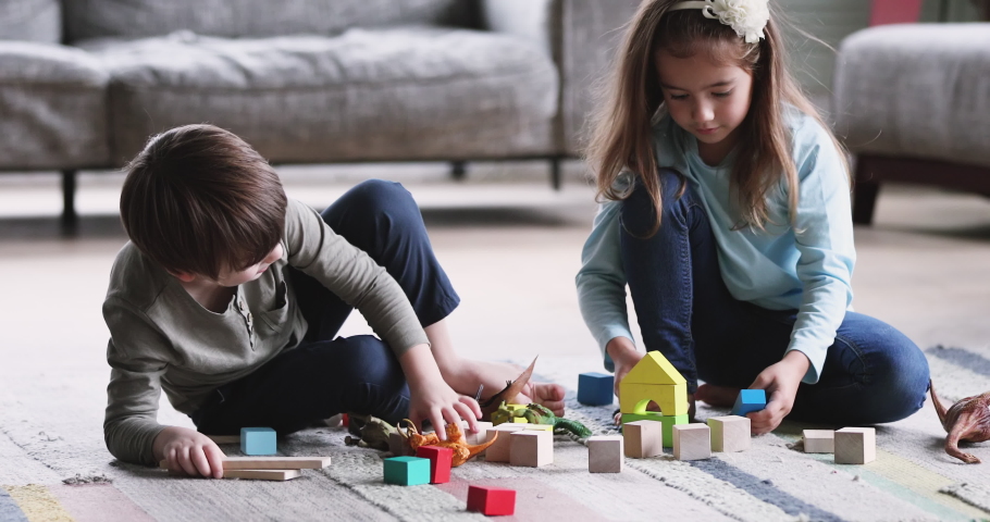 Two cute kids preschoolers brother and sister helping building of wooden blocks together sit on floor carpet. 2 friendly small siblings playing toys game in living room Royalty-Free Stock Footage #1047050956