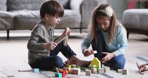 Two cute kids preschoolers brother and sister helping building of wooden blocks together sit on floor carpet. 2 friendly small siblings playing toys game in living room