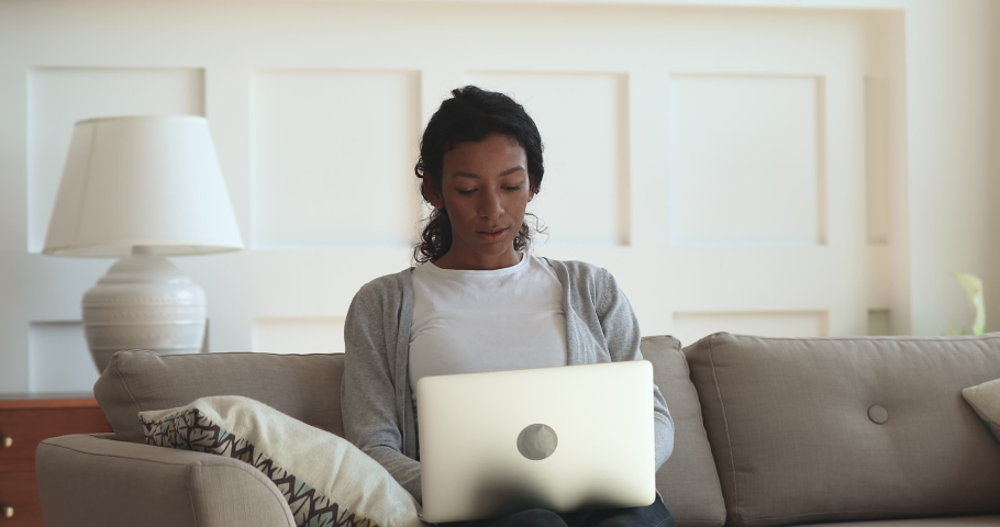Calm focused young biracial female freelancer sitting on cozy sofa, working on computer remotely at home. Concentrated african american girl studying on educational online courses, using laptop. Royalty-Free Stock Footage #1047050962