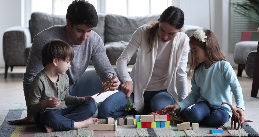 Happy carefree family, young parents mom and dad having fun play dinosaurs wooden blocks with two small preschool children. Funny kids sit on floor carpet enjoy free time game in living room together Royalty-Free Stock Footage #1047050974