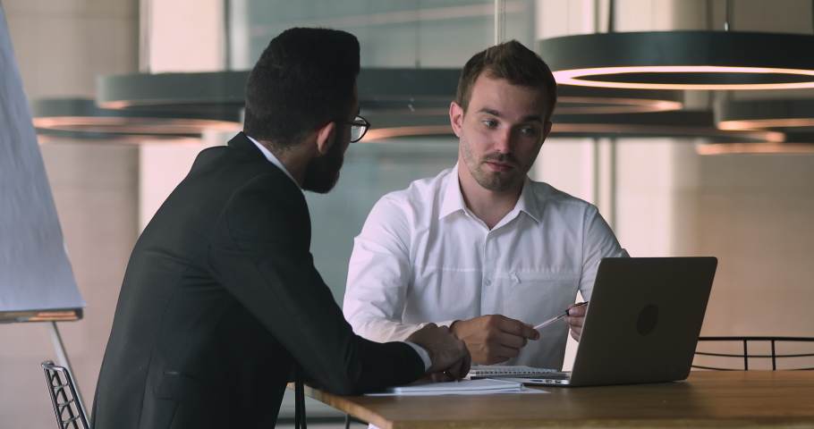 Confident caucasian male financial advisor bank worker broker explaining deal benefits, showing presentation on computer to focused arabic businessman, shaking hands after making agreement in office. Royalty-Free Stock Footage #1047050998