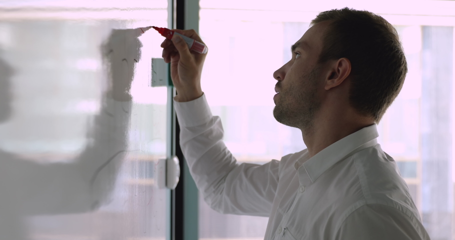Head shot side view concentrated young caucasian male manager writing notes on white board. Focused professional speaker preparing for project presentation, drawing charts on flipchart in office.