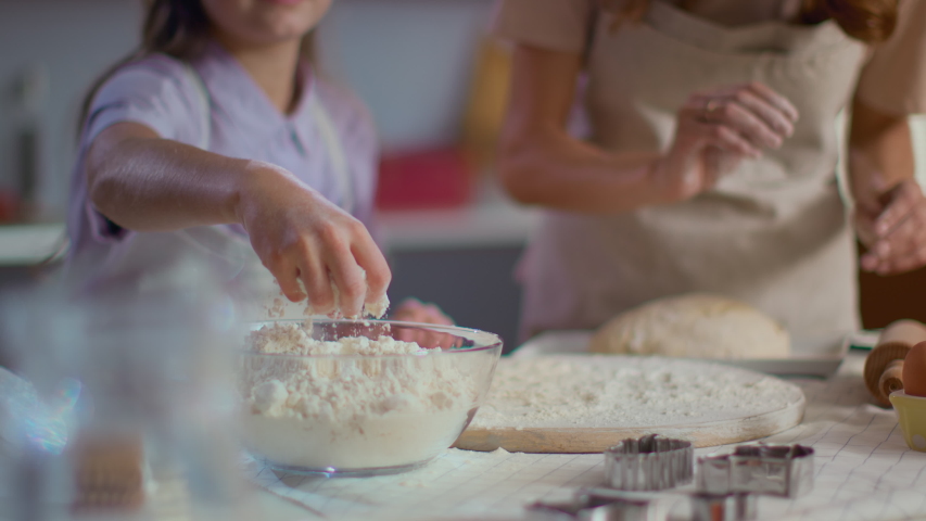 Closeup of woman and girl sprinkling flour on table at kitchen in slow motion. Mother and daughter cooking dough for cookies on modern kitchen. Family spending time together at home Royalty-Free Stock Footage #1047051190