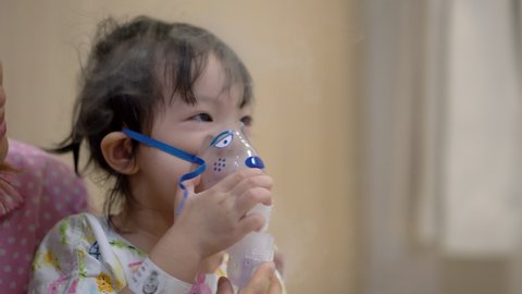 Little asian girl having a medical inhalation treatment with a nebulizer at the hospital, Little girl is resisting wearing a nebulizer. Handheld shot and Real life.