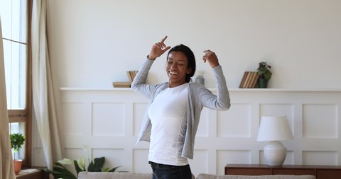 Overjoyed young african woman feeling joyful, thanking god for good luck. Thankful mixed race girl enjoying freedom alone at home. Excited homeowner spinning with stretched arms, real estate concept.