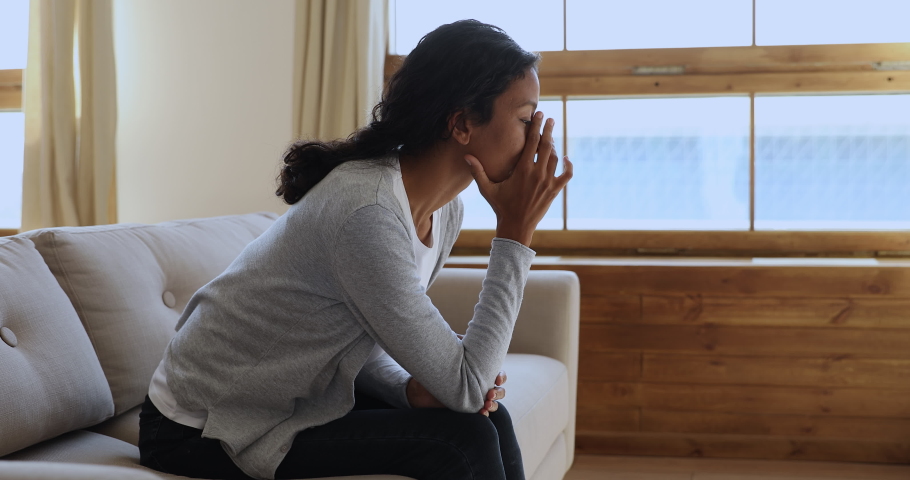 Side view stressed millennial mixed race woman lost in thoughts, sitting on cozy couch at home. Frustrated depressed young biracial girl thinking of psychological problems, relations trouble. | Shutterstock HD Video #1047056857