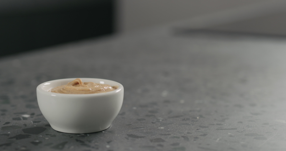 Slow motion man hand dip grissini in cashew paste in white bowl on terrazzo countertop