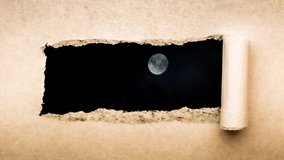 Creative 4k time laps video of a glowing full moon in the night sky with floating clouds, which is visible through a hole with torn edges in old retro grunge vintage paper.