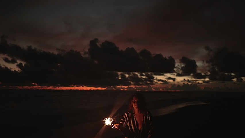 Close up portrait of young beautiful woman at sunset on beach. Pretty girl dancing in with sparkler at sunset in slow motion. Holiday with fireworks. City people travel. Business woman at vacation.