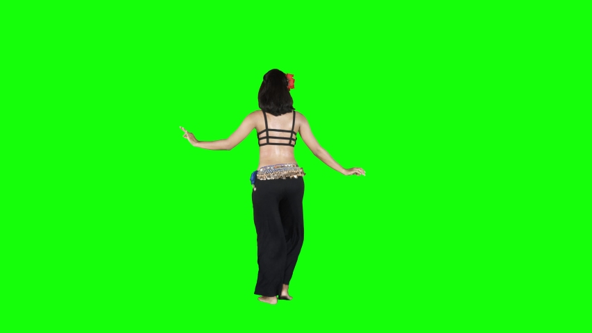 Full length view of young woman dancing and shaking her hip while doing belly dances in the studio. Shot in 4k resolution with green screen background