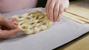 Close POV video of a woman’s hands twisting flat lengths of puff pastry on grease proof paper, to form cheese twists / straws, prior to coating and baking.