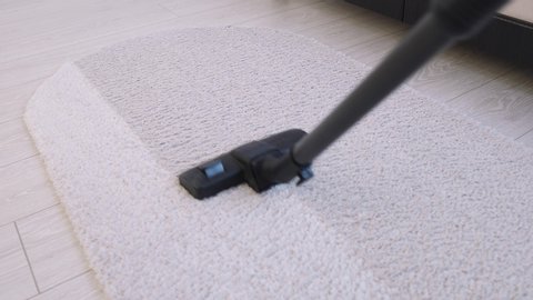 Woman using a vacuum cleaner to clean a carpet on a laminate in a home interior