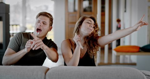 young couple singing on a sofa, slow motion of a couple singing and having fun indoor at home