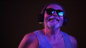 Stock footage of a cool aged man in hipster hat, sunglasses and tank top listening to music via headphones and singing along, dancing. Isolate on dark background.