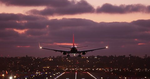 An aircraft descends from the beautiful pink and purple sunset sky and land on the runway in the big international airport, spectacularly lit with countless number of colorful lights. San Diego. 4K