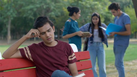 Unhappy Indian guy is very disappointed by his exam results - education failure. A young college student is sad and depressed after failing the examination while his classmates are celebrating succ...