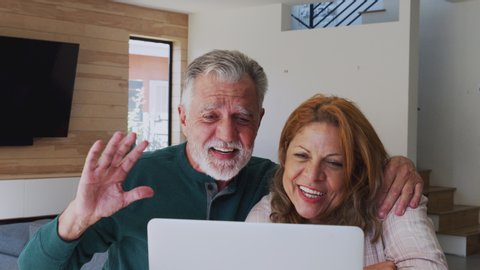 Senior Hispanic Couple At Home With Laptop Having Video Chat With Family