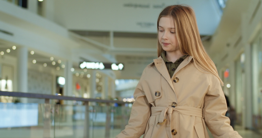 Caucasian cheerful small cute girl smiling happily to camera and showing bags after shopping in mall. Little teen kid demonstarting packets in shop. Shopper in childhood. Children consumerism concept.