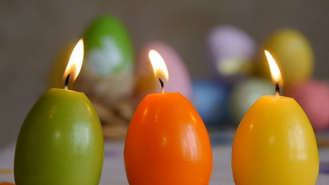 Candles made in shape of easter egg. Burning candles. Green, orange, yellow. Easter eggs candles and colorful Easter eggs in the background.