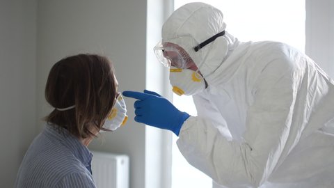 Close up portrait of a masked man in a protective suit examines an infected woman. Symptoms of Coronavirus Covid19